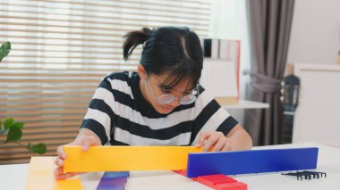 Asyalı kız, BTMM öğrenme etkinliğinin bir parçası olarak renkli bir plastik yapıyı tornavidayla birleştiriyor. Elle eğitim, çocuk mühendisliği, yaratıcılık ve sorun çözme kavramı.