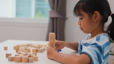 Genç Asyalı kız tahta blokları istiflemeye, STEM öğrenimini, yaratıcılığı ve motor beceri gelişimini teşvik etmeye odaklandı. Erken eğitim kavramı, problem çözme ve bilişsel büyüme.