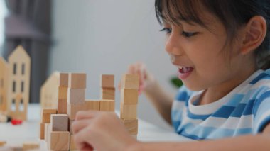 Genç Asyalı kız tahta blokları istiflemeye, STEM öğrenimini, yaratıcılığı ve motor beceri gelişimini teşvik etmeye odaklandı. Erken eğitim kavramı, problem çözme ve bilişsel büyüme.