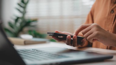 Bilgisayarda çalışırken akıllı telefon kullanan, dijital iletişimi, mobil verimliliği, akıllı ofisi, çoklu görevi ve uzak çalışma yaşam tarzını temsil eden kişiye yakın çekim.