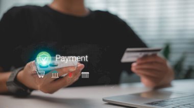 Güvenli çevrimiçi ödeme için akıllı telefon ve kredi kartı kullanan kişi, mobil bankacılık, e-ticaret, finans teknolojisi ve küresel dijital işlem sistemini temsil eden holografik simgelerle.