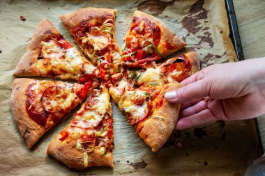 Kadın eli, ev yapımı pizza dilimini kabartma kağıdının üzerine alıyor. Üst görünüm