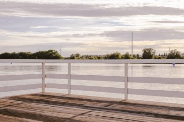 Beyaz Tahta Raylı Jetty Gölü ve Uzakta Rüzgâr Türbinleriyle Suyun Üzerinde Gün Batımı Manzarası