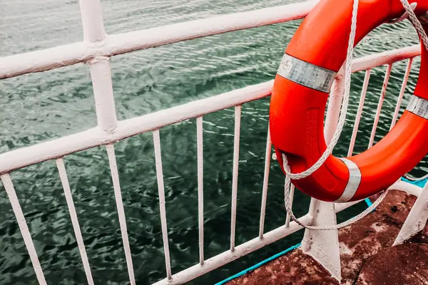 Pright Red Lifebuoy Arkaplanda Derin Turkuaz Suyu ile Beyaz Metal Feribot Demiryollarında Asılı