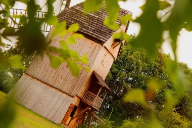 Etrafı yapraklarla çevrili eski ahşap yel değirmeni yeşil kırsal alanda