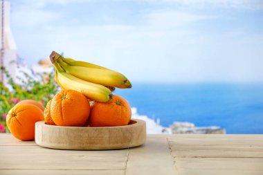 Fresh fruit  on a wooden plate bowl on white wooden board table top with blurred bright sea background clipart