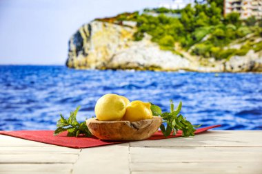 Masaya dağılmış sarı limonlar ve arka planda güzel bir okyanus, dağlık kayalar ve adalar ve berrak gökyüzü..