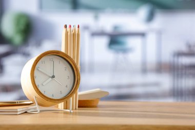 Bir çalar saat ve okul malzemeleri okul içindeki bir sınıfın ahşap masasında ürünler için yer var. Tebeşir duvarlı arka plan. Okul zamanı. Okul malzemeleri ve aksesuarları için yer var..