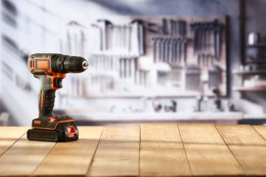 Elektrik kablosuz matkap, tornavida aleti el sanatları atölyesindeki ahşap çalışma masasında. Arka planda aletler olan bulanık bir duvar. Ürün montajı için zanaat konsepti ve boş reklam alanı.
