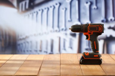 Elektrik kablosuz matkap, tornavida aleti el sanatları atölyesindeki ahşap çalışma masasında. Arka planda aletler olan bulanık bir duvar. Ürün montajı için zanaat konsepti ve boş reklam alanı.
