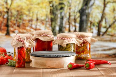 Sonbahar sebze turşuları sonbahar masasında cam kavanozlarda ve ürünler için boş bir yer. Arka planda, sarı ve turuncu yapraklı bir sonbahar ormanı ağaçları var..