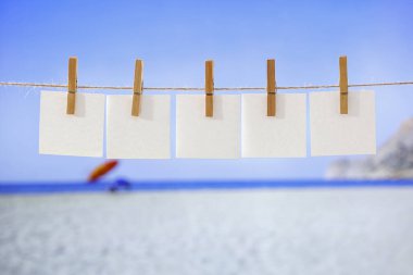 Mavi deniz arka planında çamaşır mandalları olan boş beyaz elbise etiketi. Çamaşır konsepti. Boşluğu kopyala.