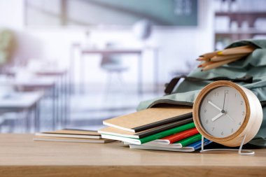 Okul masasında saat, sırt çantası, renkli kalemler ve not defterleri vardı..