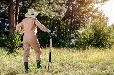 Sıcak sonbahar güneşli bir günde bahçede yürüyen çiftçi. Yeşillik, çimenler ve ağaçlar. Sonbahar bahçıvanlığı.