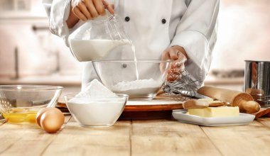 Mutfaktaki ahşap masada yemek pişiren ve hamur yapan beyaz şef üniforması giyen bir kadın. Ürünler için alanı kapat ve kopyala.