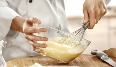 Kadın elleri mutfakta yemek pişirir ve yemek hazırlar. Beyaz aşçı üniformalı kadın mutfaktaki masada lezzetli hamurlar yapıyor. Mutfak içi arka plan.