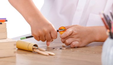 Beyaz gömlekli bir öğrenci küçük, sarı bir kalem açacağı kullanarak kalem keskinleştiriyor..