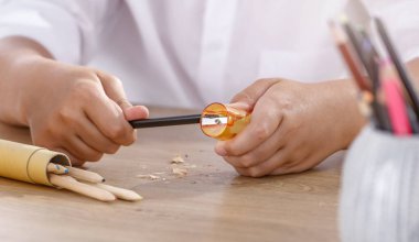 Beyaz gömlekli bir öğrenci küçük, sarı bir kalem açacağı kullanarak kalem keskinleştiriyor..