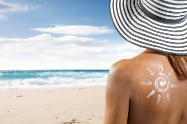 Plajda güneş koruyucu şapkalı bir kadın. Mavi deniz ve gökyüzü arkaplanı.