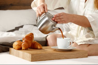 Kadın yatakta kahvaltı yapıyor. Kadın elleri beyaz bir fincana kahve dolduruyor..