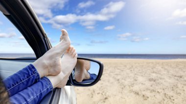 Plajda araba camından sarkan bacaklar - yaz gezisi yaşam tarzı. Marka ya da metin yerleştirme için boş alan. Rahatlatıcı sürüş ve seyahat özgürlüğü kavramı.