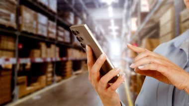 Ekranda, bulanık bir depo arkaplanı ile görülebilen mesaj için boş yeri olan telefonu tutan kadın çalışan. Ürün ve lojistik ve e-ticaret konsepti için alanı kopyala.