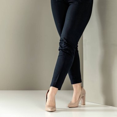 Siyah pantolonlu kadın bacakları ve açık arkaplanda yüksek topuklu ayakkabılar.