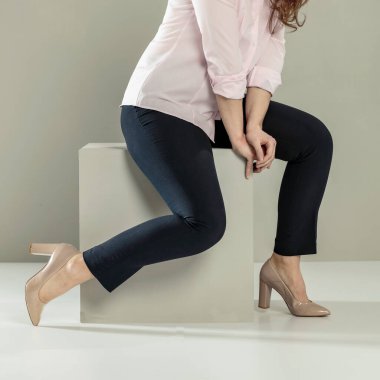 Koyu renk pantolonlu, manken pozu giymiş genç bir kadın. Fotoğraf montaj görüntüsü için kullanılabilecek vücut parçaları. Arkaplan tarafsız, basit bir ayar sağlıyor. Yüksek topuklu giyen kadın