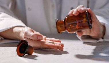 Kadın doktor elleri cam bir şişe tutuyor ve masada hapları gösteriyor. İlaç ve hastalık tedavi konsepti. Ürün ve metin için alanı kopyala.