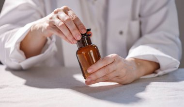 Kadın doktor ya da eczacı ellerinde hafif arka planda haplar olan bir şişe tutuyor.