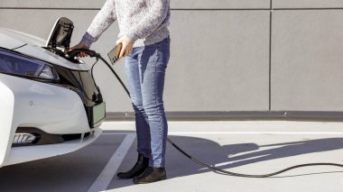 Kadın şarj istasyonunda elektrikli araba takıyor. Çevre dostu ulaşım konsepti. EV şarj oluyor ve sürdürülebilir enerji ve yeşil teknolojiyi destekliyor.
