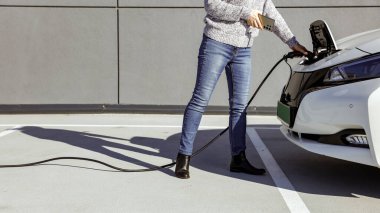 Kadın şarj istasyonunda elektrikli araba takıyor. Çevre dostu ulaşım konsepti. EV şarj oluyor ve sürdürülebilir enerji ve yeşil teknolojiyi destekliyor.