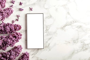 Bahar kompozisyonu içinde leylaklarla fotokopi alanı olan boş ekran cep telefonu. Düz konum ve beyaz mermer arkaplan modeli.