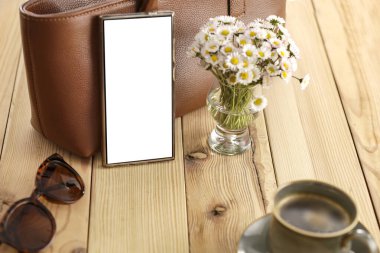  Hoş bir kompozisyon, papatya çiçekleri ve ahşap masa üzerine kadın çantası, rahat bir arka plan. Metin veya ürün için kopyalama alanı olan boş ekranlı akıllı telefon. Anneler Günü, Kadınlar Günü, doğum günü tebriği veya bahar tasarım projesi kartı.