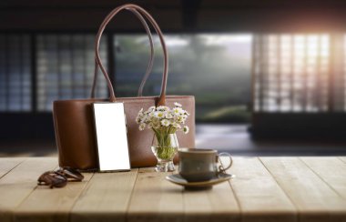 Papatya çiçekleri, kahve fincanı ve cam kenarı bulanık ahşap masa üzerindeki kadın çantasıyla zarif bir bahar kompozisyonu. Anneler Günü, Kadınlar Günü ve tasarım proje kartı için metin ya da ürün alanı olan akıllı telefon ekranı.