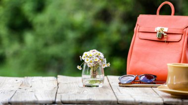 Tahta masadaki bahar kompozisyonu papatya çiçeği buketi, fincan, çay tabağı, akıllı telefon ve bulanık bahçeye ayarlanmış el çantası. Anneler Günü ya da Kadınlar Günü ya da fotokopi alanı olan tebrik kartı geçmişi.