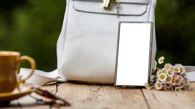 Mesaj, beyaz poşet, kahve bardağı, kahve fincanı, çiçekler, yeşil yapraklar ve bulanık arkaplan için fotokopi alanı olan boş akıllı telefon ekranı. Anneler Günü ya da Kadınlar Günü ya da fotokopi alanı olan tebrik kartı geçmişi.