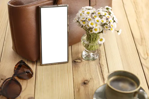  Hoş bir kompozisyon, papatya çiçekleri ve ahşap masa üzerine kadın çantası, rahat bir arka plan. Metin veya ürün için kopyalama alanı olan boş ekranlı akıllı telefon. Anneler Günü, Kadınlar Günü, doğum günü tebriği veya bahar tasarım projesi kartı.