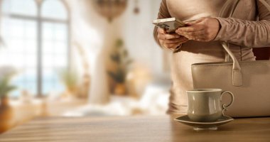 Sabah Rutinini El Çantası ve Kahveyle Bırakmadan Önce Telefonu Kontrol Eden Kadın. Günlük Yaşam Tarzı Sahnesine Çıkmadan Önce Akıllı Telefon Kullanıyor.