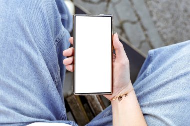 Akıllı telefon, genç bir bayanın elinde güneşli bir parktaki ahşap bankta oturuyor. Modern teknolojiyle doğal çevreyi harmanlayan kavramsal bir görüntü. Metin için alanı kopyala.