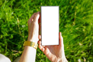 Açık ekran ve boş ekranlı akıllı telefon. Doğal yeşil bahçe arka planında güpegündüz çimen ve doğal yapraklarla yazı yazmak için yer var. Boşluğu kopyala.