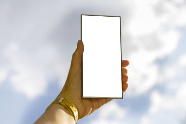 Akıllı telefonlu ve ekranı boş olan bir kadın. Gökyüzü arka planında gün ışığında güneşli bir yazı için yeri var..