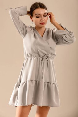 Açık gri duvarın önünde poz veren genç bir kadının stüdyo portresi. Tarafsız arka plan ve yumuşak ışıklandırma ve çok yönlü görünüm moda editörleri, model portföyleri, reklam modelleri veya minimalist güzellik ve yaşam tarzı kavramları için uygundur..