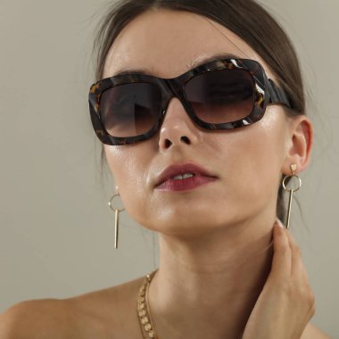 Açık gri bir duvarın önünde poz veren genç bir kadının portresi. Tarafsız arka plan ve yumuşak ışıklandırma. Moda başyazıları, model portföyleri, reklam modelleri veya minimalist güzellik ve yaşam tarzı kavramları için görüntü.