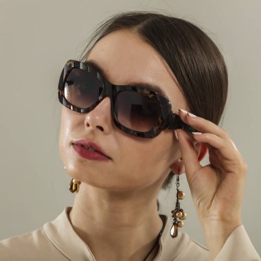 Açık gri bir duvarın önünde poz veren genç bir kadının portresi. Tarafsız arka plan ve yumuşak ışıklandırma. Moda başyazıları, model portföyleri, reklam modelleri veya minimalist güzellik ve yaşam tarzı kavramları için görüntü.