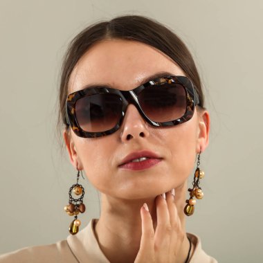 Açık gri bir duvarın önünde poz veren genç bir kadının portresi. Tarafsız arka plan ve yumuşak ışıklandırma. Moda başyazıları, model portföyleri, reklam modelleri veya minimalist güzellik ve yaşam tarzı kavramları için görüntü.