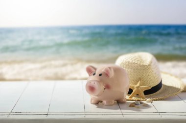 Yaz tatili. Kumsalda kumsalda oyuncak bir kumbara ve hasır şapka. Bulanık plaj, deniz ve gökyüzü arka planı, ürün yerleştirme ve metin için alan. İş ve tatil konsepti için para biriktirme.