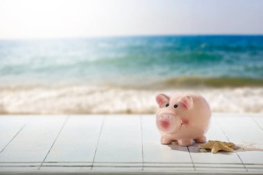 Ahşap masanın üzerinde, deniz kenarı geçmişi olan pembe bir kumbara. Bulanık plaj, deniz ve gökyüzü arkaplanı, ürün yerleştirme ve metin için alan