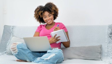Evde bilgisayar başında Afro-Amerikan bayan öğrenci öğreniyor.