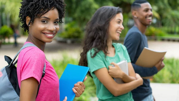 アフリカ系アメリカ人の女子学生を笑いながら 都会で夏に屋外で若い大人のグループと — ストック写真